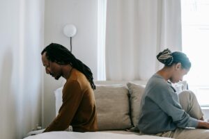 Stressed black couple sitting on bed in misunderstanding causing distance in the relationship