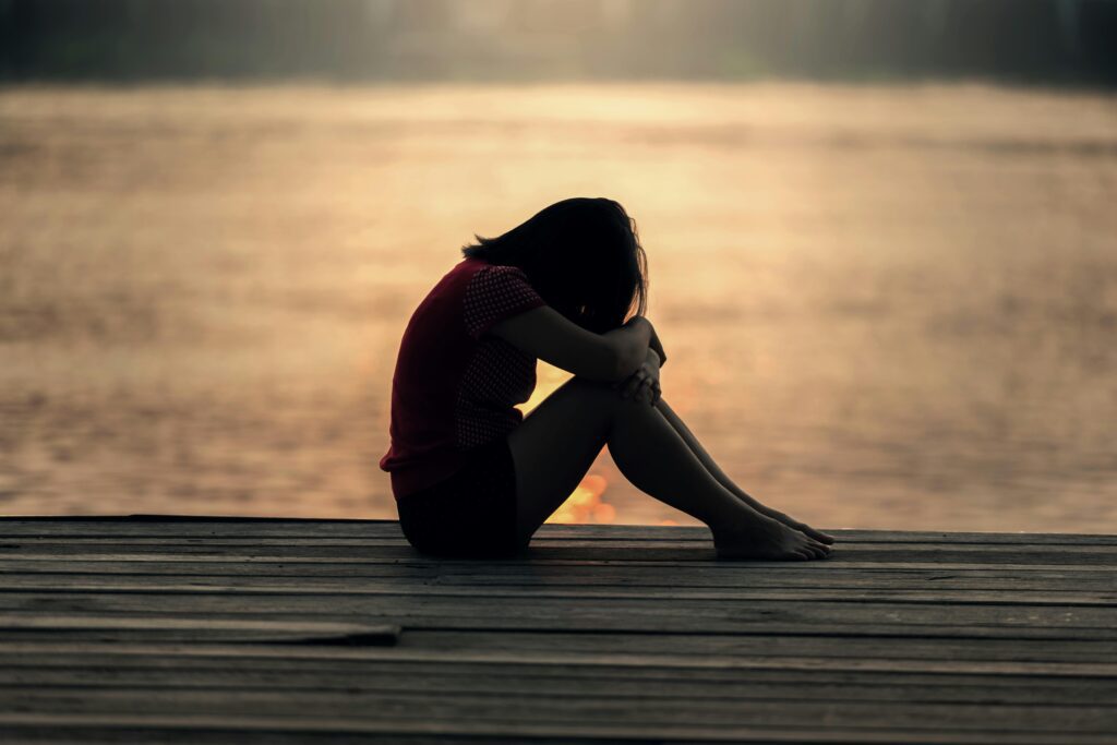 A silhouette of a person sitting on a dock at sunset, reflecting in solitude. The peaceful setting symbolizes reducing stress and embracing peace in quiet moments.